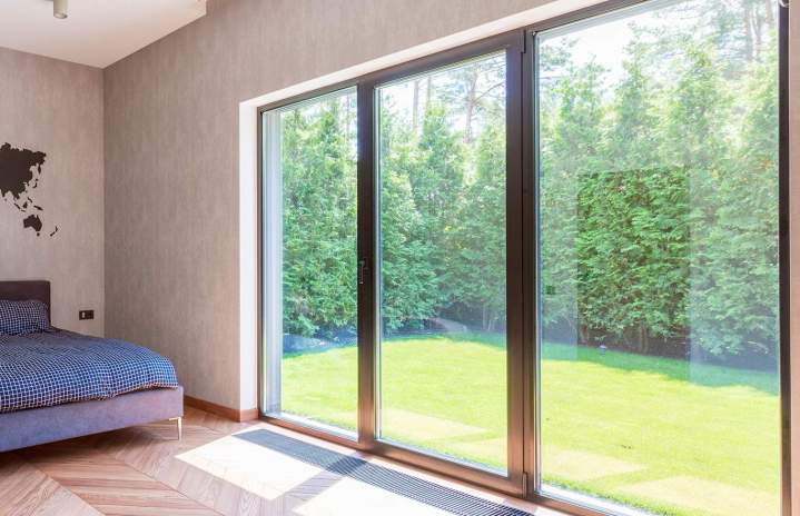 Baie vitrée de grande largeur à cadre foncé et trois parties vitrées, ouverte sur un jardin depuis une chambre