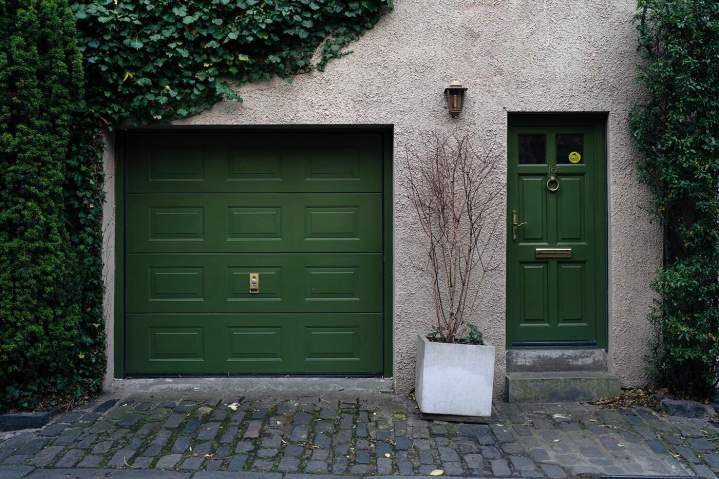Porte de garage sectionnelle verte sur façade de maison de caractère avec pavés