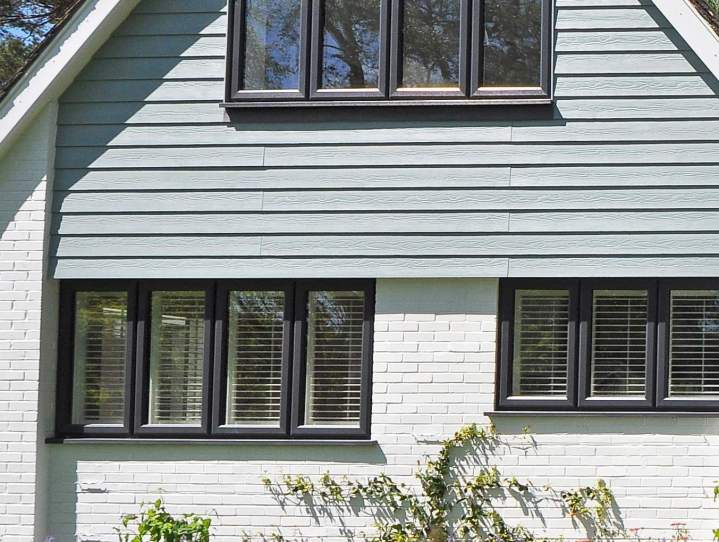 Fenêtres aluminium anthracite avec persiennes à lames sur façade bardage gris et brique blanche, maison individuelle
